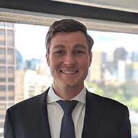 A smiling Mark Strauss stands confidently in a suit, framed against a breathtaking cityscape in the background.