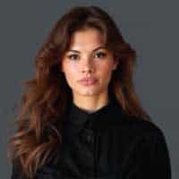 Fridah Muthoni, a young woman with long brown hair wearing a black button-up shirt, stands against a plain gray background.