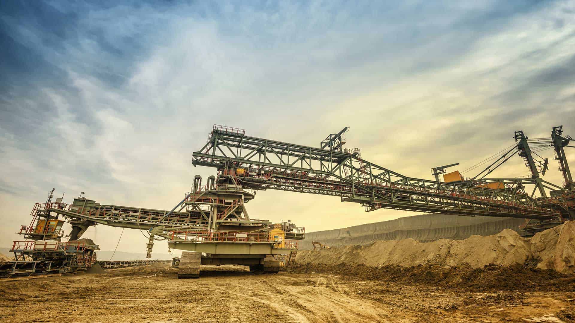 A large industrial excavator machine operates in an open-pit mine under a cloudy sky.