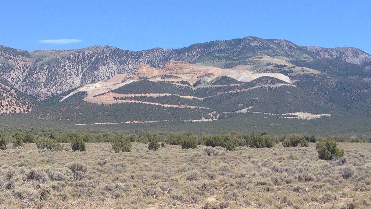 Landscape view of a mountain with visible layers of exposed rock and sparse vegetation in the foreground under a clear blue sky.